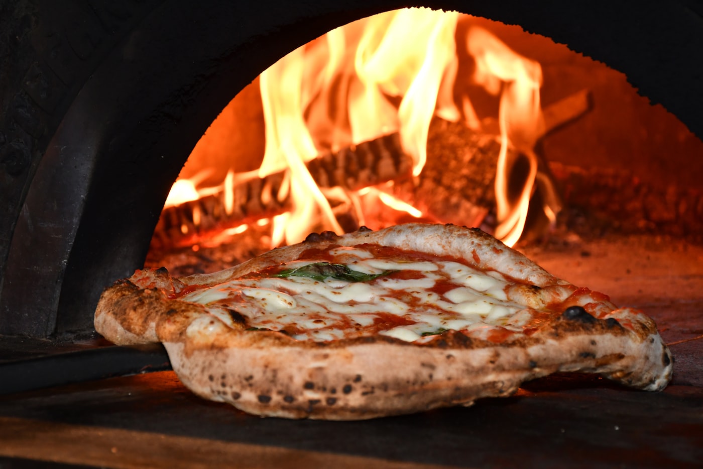 Une margherita glissée à la pelle sur la sole du four à bois, léchée par la flamme