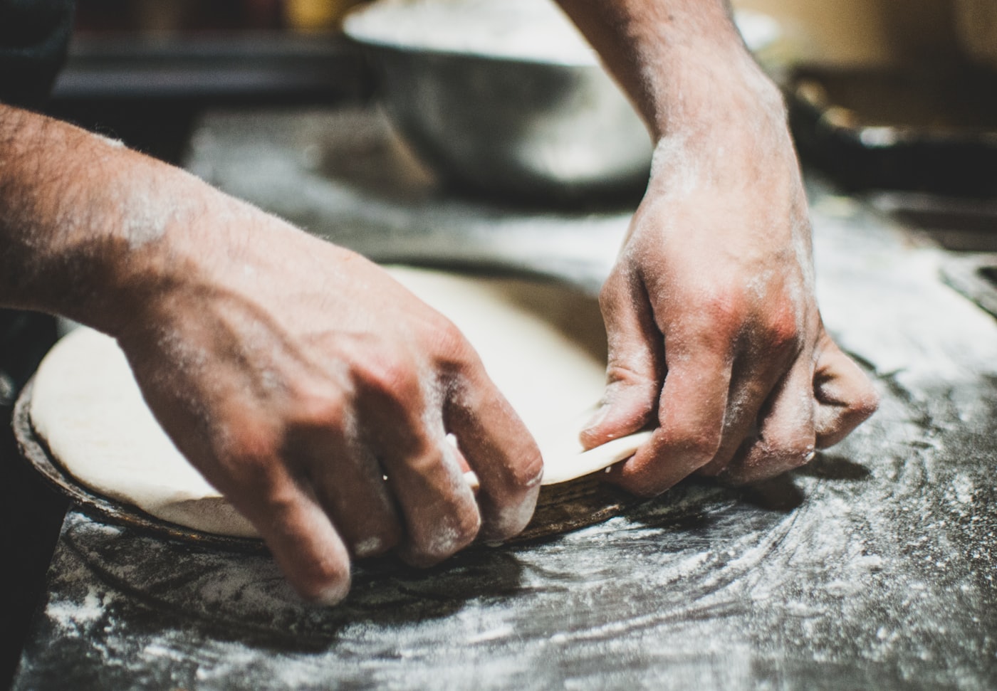 Les mains du pizzaïolo étirent un disque de pâte sur le plan de travail fariné