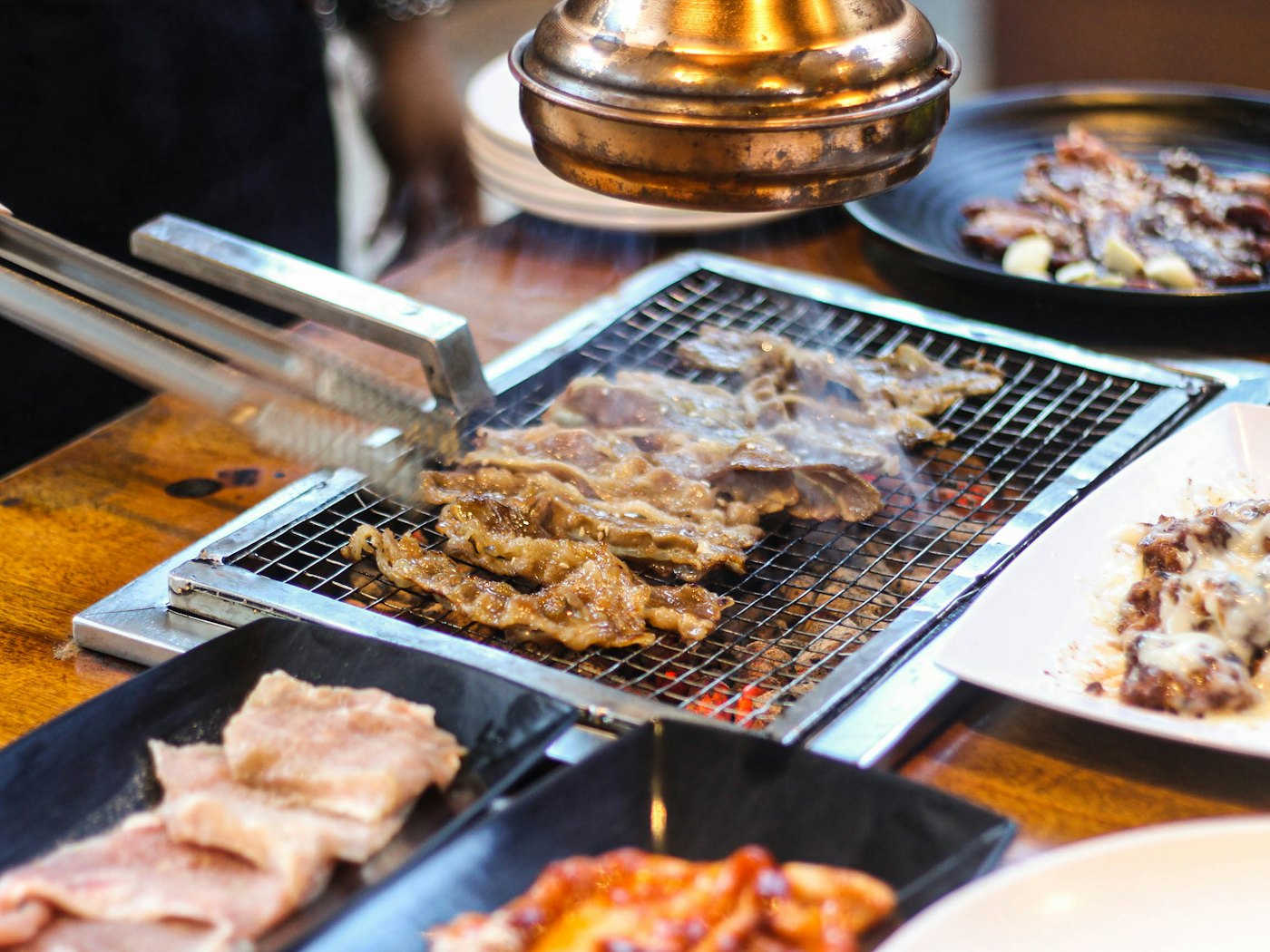 Pièce de galbi saisie sur le grill au charbon, retournée à la pince au-dessus des braises