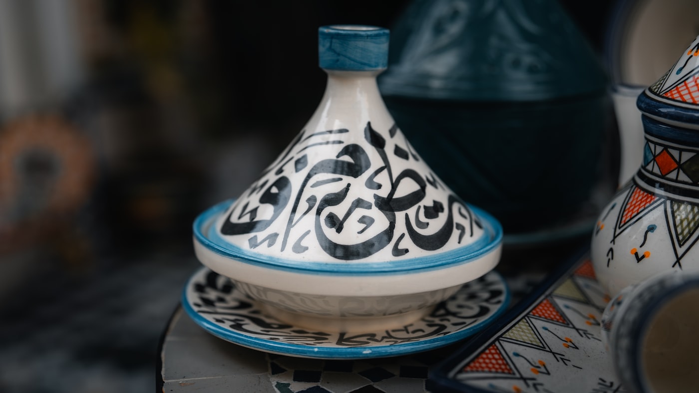 Tajine de service en céramique blanche et bleue, orné de calligraphie arabe, posé sur une table en zellige