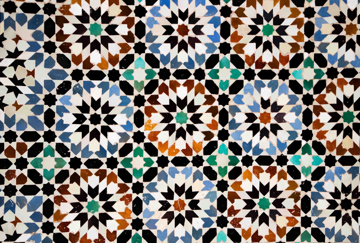 Mosaïque de zellige marocain en plein cadre : étoiles géométriques imbriquées, émaux bleus, bruns, verts et blancs taillés à la main
