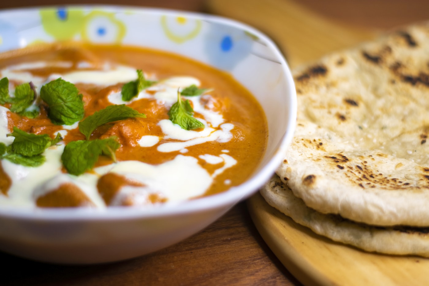 Butter chicken crémeux aux tons dorés, garni de menthe fraîche, un naan posé au bord de l'assiette.