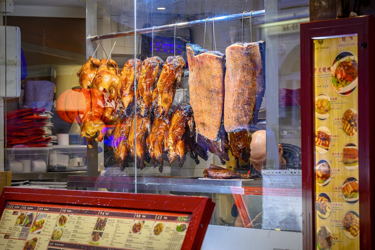 La devanture du restaurant la nuit&nbsp;: viandes laquées suspendues derrière la vitre, lanterne rouge allumée, menus rétroéclairés.